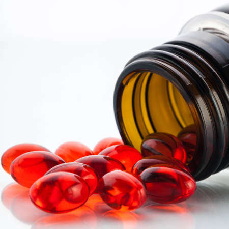 Transparent red oil capsules with vitamin E poured out of bottleの写真素材