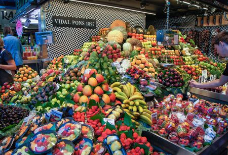 Barcelona market, Spain - August 1, 2015.Man examining fruits pyramid stacked on the counter.のeditorial素材