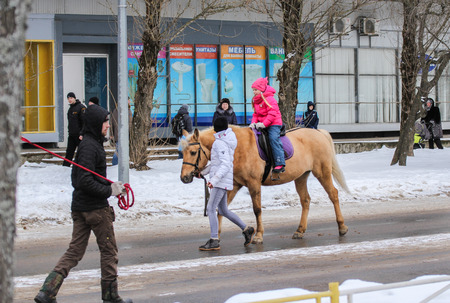 Girl riding a horse. People in the city at the traditional national holiday of Maslenitsa.のeditorial素材