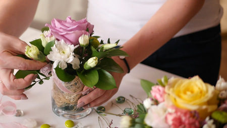 Florist girl collects a nice little bouquet of roses and other flowers in a small vaseの写真素材