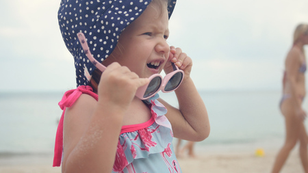 A little sweet girl in a choca in polka dots, playing with children's sunglasses.の写真素材