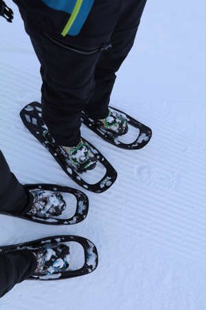 2 pairs of feet in the snow wearing snow shoes