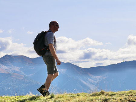 hiker with a day pack walking in a green mountain meadow with hazy blue mountains in the distanceの写真素材