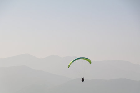 paraglider in the air with a colorful parachute in monochrome background of a hazy mountain range in...