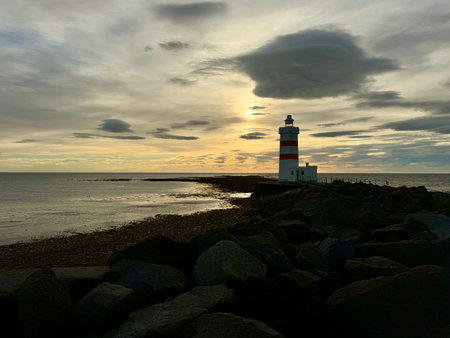 silhouette of a lighthouse at the end of a breakwater with clouds in the colorful evening sky at sunsetの写真素材