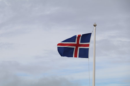 Icelandic flag flying on a flag pole with a cloudy sky behindの写真素材