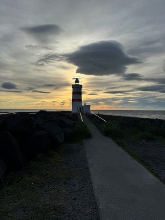 Old Gardur lighthouse at sunset with a dark path leading to the lighthouse and orange and blue shaded in the partly clouded skyの写真素材