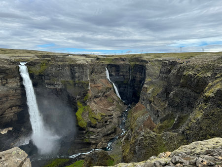 panoramic view of Haifoss and Grannifoss plummet off a flat treeless plateau into a canyon showing different geological layers of stoneの写真素材