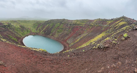 panoramic view of Kerid volcanic crater with turquoise crater lake and red rock mossy slopes with...