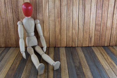 wooden man with a red head sitting on wood background textureの写真素材
