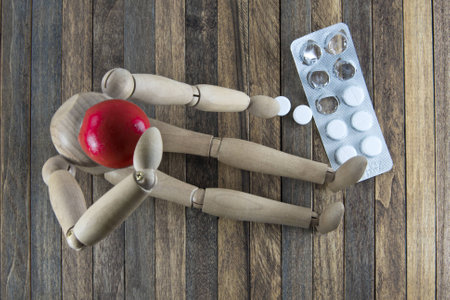 Wooden men sitting on a wooden Desk and holding his hands behind his head and lay next to white pillsの写真素材