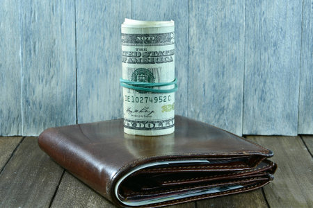 brown men's wallet and dollars on wooden background