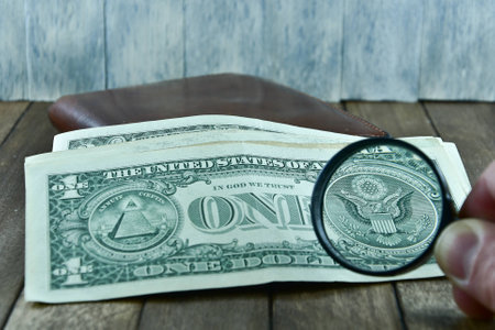 brown men's wallet and dollars on wooden background