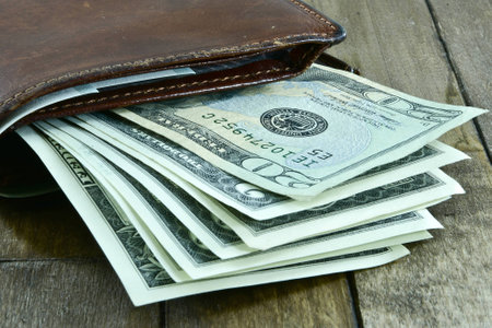 brown men's wallet and dollars on wooden background