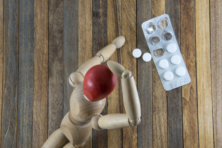 Photo of Wooden man with a red head (headaches) crawling to tabletsの写真素材