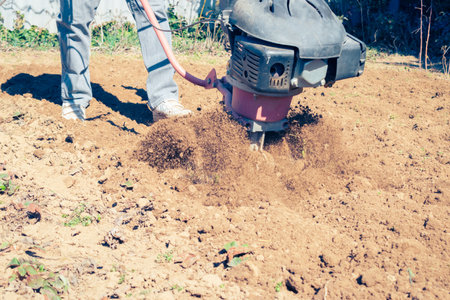 Farmer plows the land with a modern mechanical rotary tiller on a sunny spring day in the countrysideの写真素材