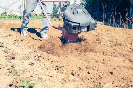 Farmer plows the land with a modern mechanical rotary tiller on a sunny spring day in the countrysideの写真素材