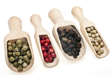 Four different kinds of peppercorns in wooden spoons on a white 