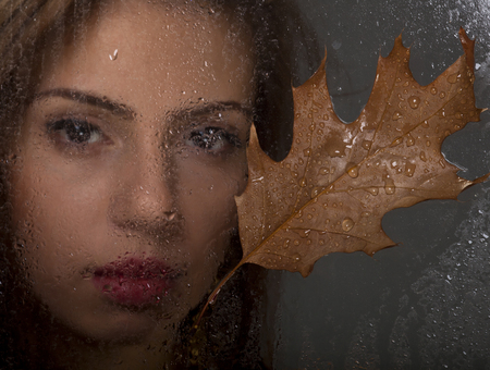 Beautiful girl looks out of the window with raindrops.の写真素材