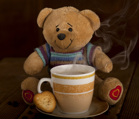 Sweet Teddy bear with cup of coffee, hot chocolate or tea and cookie in heart shape on brown wooden background.の写真素材