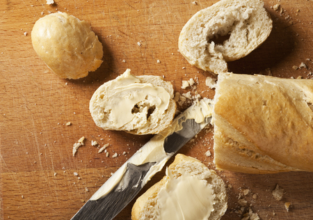 French bread baguette and its slices with butter and metal knife on wooden の写真素材