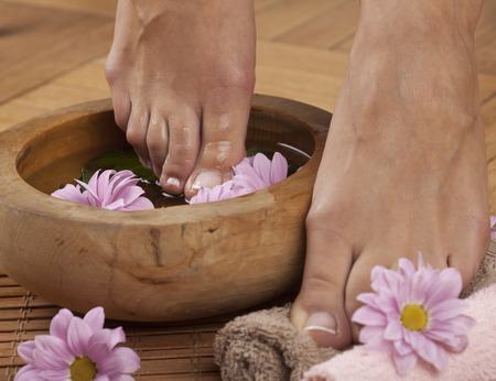 Feminine feet in foot spa bowl with flowers and towelsの写真素材