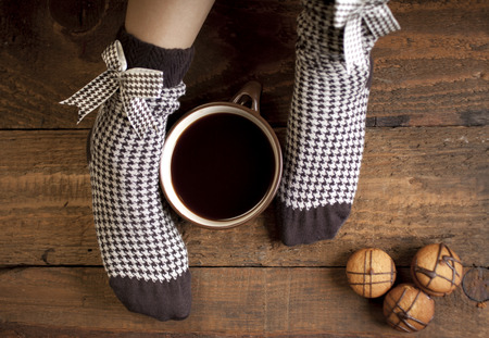 A cup of coffee or hot chocolate and female feet with sweet brown socks on a wooden background.の写真素材