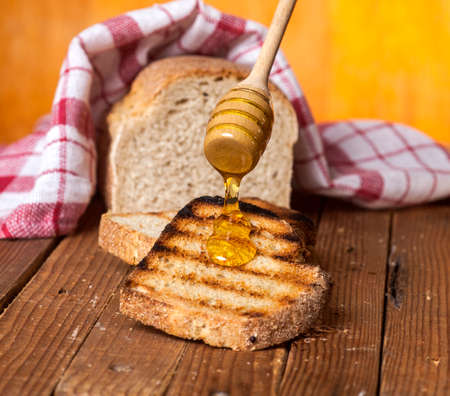 Toasted bread with honey and honey dipper on a wooden background.の写真素材