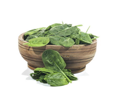 Green spinach in wooden bowl on a white background