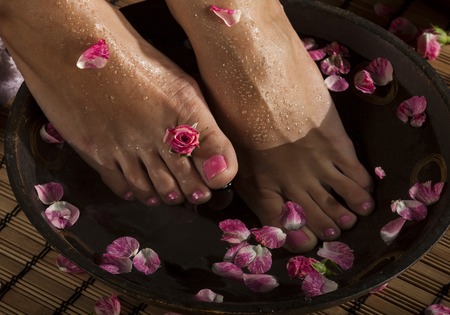 Female feet with drops of water in spa bowl with water and roses.の写真素材