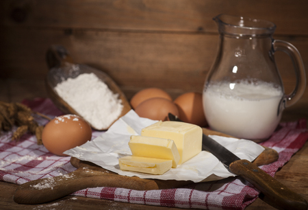 Ingredients for the preparation of bakery products: flour eggs butter milk wheat spikes. Rustic style. Brown wooden background.の写真素材