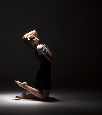 Modern female dancer dancing with face mask on dark background. Conceptual photoの写真素材