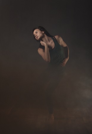 Young beautiful dancer in black leotard dancing on a gray smoke studio backgroundの写真素材