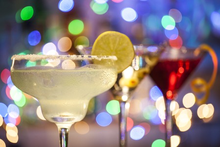 Glasses of margarita, martini and cosmopolitan cocktails on bar lights background with copy spaceの写真素材