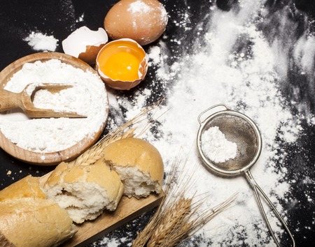 Ingredients and utensils for the preparation of bakery products - flour, eggs, spoon, bowl, bread -...