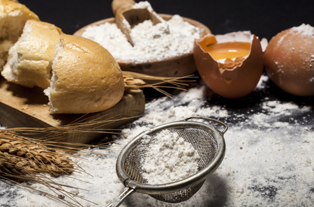 Ingredients and utensils for the preparation of bakery products - flour, eggs, spoon, bowl, bread - on black table with free copy spaceの写真素材