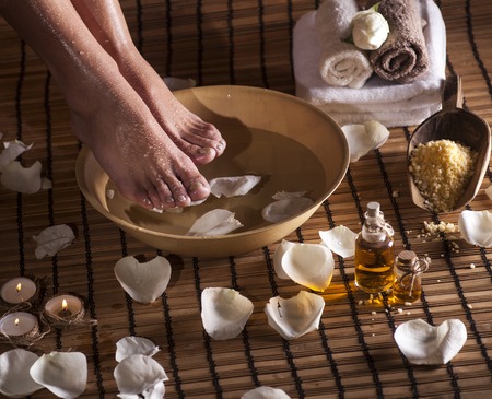 Female feet with drops of water, spa bowl, towels, flowers, candles, sea salt and bottle with essential oil. Foot spa concept.の写真素材