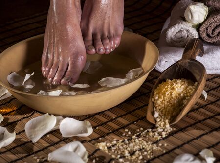 Female feet with drops of water, spa bowl, towels, flowers, candles, sea salt and bottle with essential oil. Foot spa concept.の写真素材