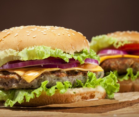 Fresh delicious burgers with meatball, cheese, tomato, onion and lettuce on wooden table and dark background with copy spaceの写真素材