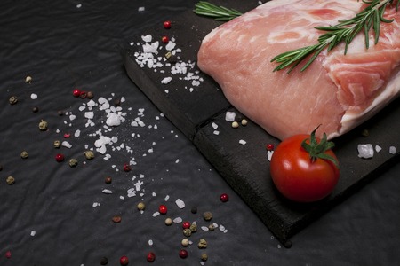 Raw meat. Raw pork meat on a cutting board with rosemary, vegetables and spices on black background.の写真素材