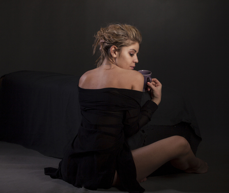 Sexy beautiful girl with cup of coffee, hot chocolate or tea sitting near the bed.の写真素材