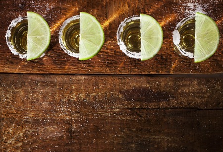 Gold tequila shots with lime fruits on wooden backgroundの写真素材