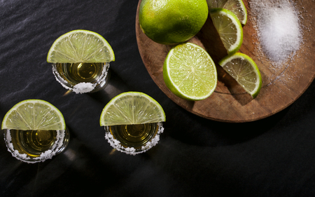 Gold tequila shots with lime fruits on black backgroundの写真素材