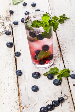 Summer cold drink with blueberry, mint and ice in glass on white wooden backgroundの写真素材