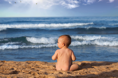Baby boy sitting on the beach near the water.の写真素材