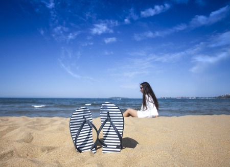 Blue sandal flip flop on a sand beach and beautiful woman in the distanceの写真素材