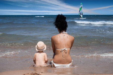 Mother and her baby boy sitting on the beach near the water.の写真素材