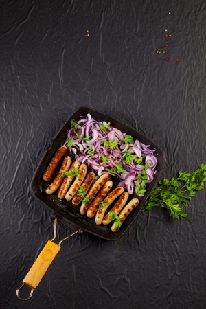 Fried sausages with parsley and onion in a pan on black backgroundの写真素材