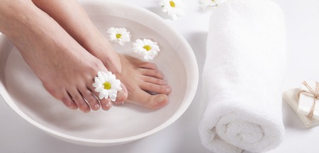 Female feet with spa bowl, towel and flowers on white backgroundの写真素材