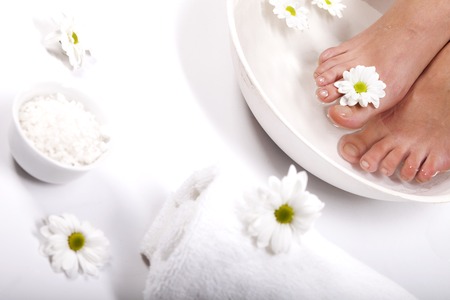 Female feet with spa bowl, towel and flowers on white backgroundの写真素材